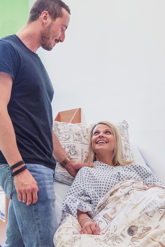 Pacientka na lůžku po zákroku s&nbsp;partnerem
