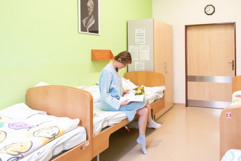 Pacientka čte na lůžku v pokoji po zákroku